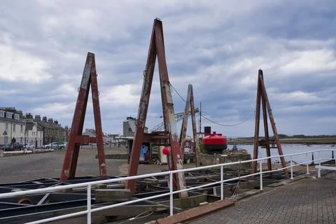 Red A-frame cranes stand tall beside a calm harbor Stock Photos
