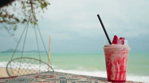 Red Fruit Smoothie on Patterned Table Beside Tropical Beach Stock Footage 347791828