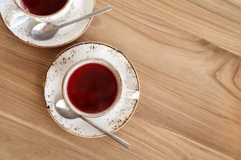 Red fruit tea in trendy ceramic white cups with brown decor on wooden table.  Stock Photos