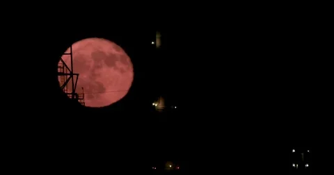 Red full moon rising from behind a large oil refinery Stock Footage 80809633