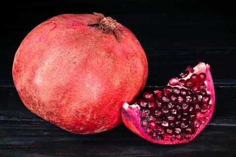 Red garnet whole and half on a black wooden table Stock Photos