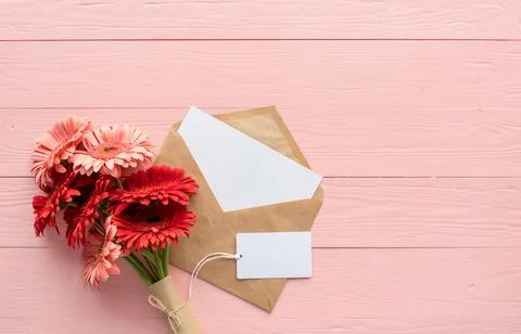 Red gerbera daisy flowers, envelope and blank label tag on pink wooden table Stock Photos