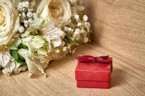 Red gift box with bow on lid, bouquet of white flowers on wooden background,  Stock Photos