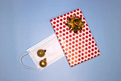 Red gift box decorated with a bow with balls and a mask on a blue background Stock Photos
