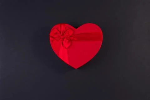 Red gift box heart shape with red ribbon on a black background, gift concept Stock Photos