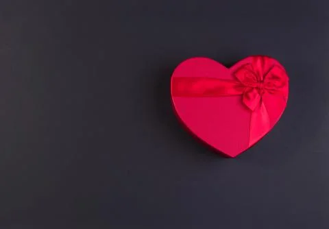 Red gift box heart shape with red ribbon on a black background, gift concept Stock Photos