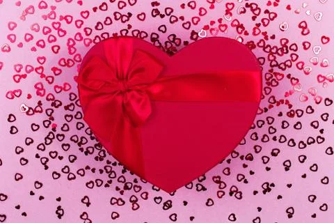 Red gift box heart shape with red ribbon on a pink sequinbackground, gift Stock Photos
