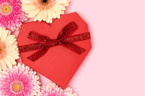 Red gift box in a heart shape and gerbera flowers on a pink background. Stock Photos
