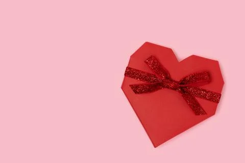 Red gift box in a heart shape with tied glittering ribbon. Stock Photos