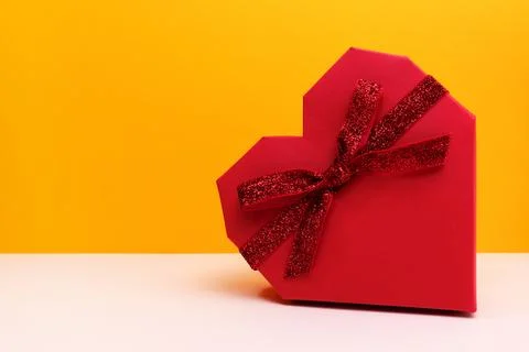 Red gift box in a heart shape with glittering ribbon bow. Stock Photos