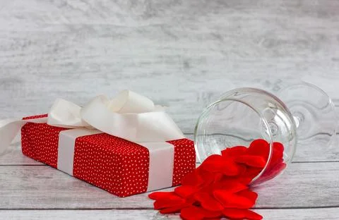 Red gift box with pea pattern, white ribbon and heart on wooden background... Stock Photos