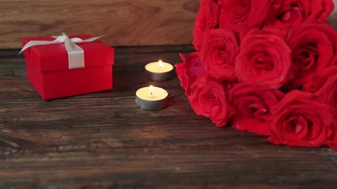 Red gift box present and ruby roses burning candles wooden table Valentines Day Video stock 166560311