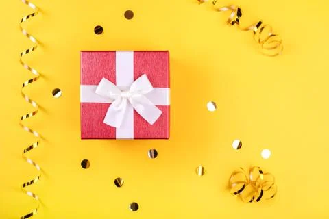 Red gift box on yellow background with golden confetti. Stock Photos