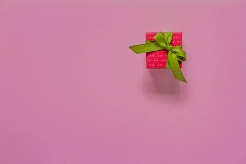 Red gift or present box with green ribbon on pink table top view. Flat lay. B Foto stock