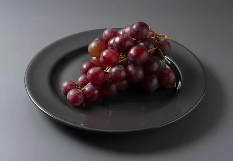Red Globe served on a plate set against a gray background. Stock Photos