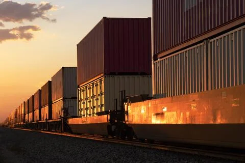 The red glow of sunset on a passing container stack train Foto stock