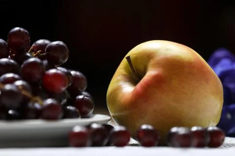 Red grape in front and apple in a back on a dark background Stock Photos