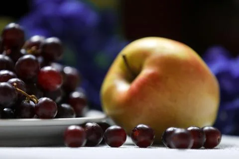 Red grape in front and apple in a back on a dark background Stock Photos