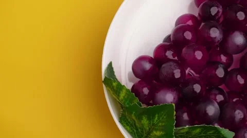 Red grape in white plate spinning on isolated yellow background Stock Footage 274043002