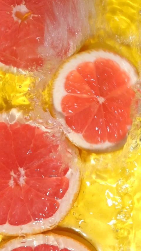Red grapefruit slice falling into liquid and splashing, vertical format. Stock Footage 341577392