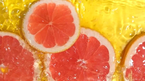 Red grapefruit slice falling into water and splashing, slow motion. Stock Footage 344952628
