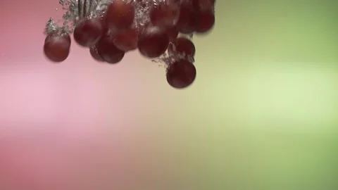 Red grapes fall into the water in slow motion. on a colored background Stock Footage 131037343