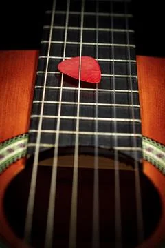 Red Guitar Pick Between the Strings of an Old Acoustic Guitar Foto stock