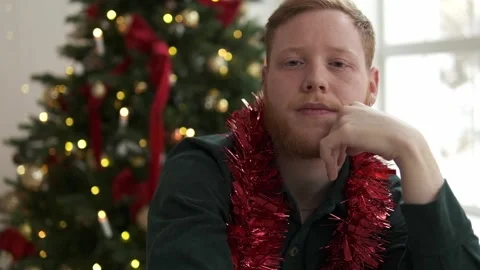 Red-haired bearded man is sitting in front of a Christmas tree Stock Footage 294038972