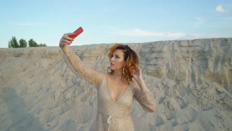 Red-haired beauty posing on the sand in front of the photographer. woman in a Stock Footage 95487227