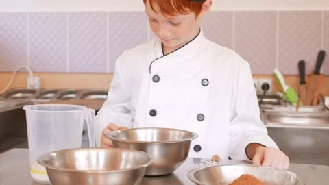 Red-haired boy in chef's costume cooks pancakes in kitchen, kneads dough Stock Footage 197066154