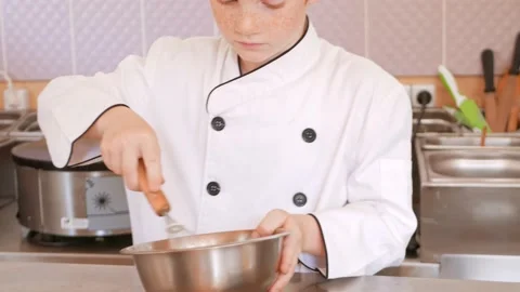 Red-haired boy in chef's costume cooks pancakes in kitchen, kneads dough Stock Footage 197066186
