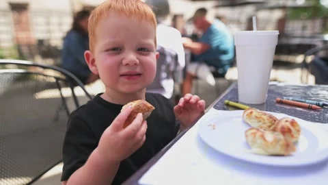 Red-haired boy eating pizza breadstick outdoors at a restaurant table Stockbeeldmateriaal 320147389