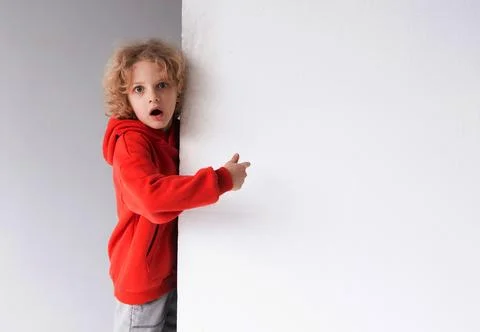 A red-haired boy in a red sweater with a surprised face points his finger a.. Stock Photos