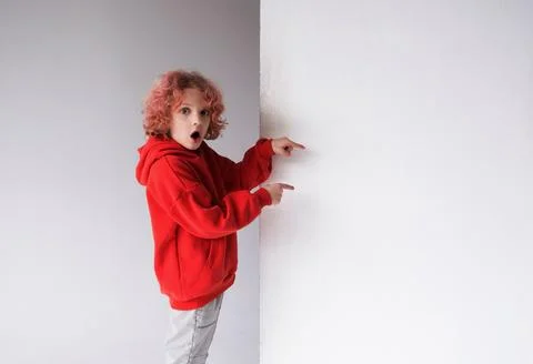 A red-haired boy in a red sweater points his finger at an empty white board,  Stock Photos