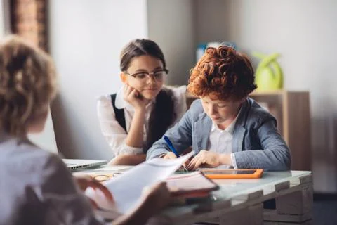 Red-haired boy studying with his friends and looking concentrated Stock Photos
