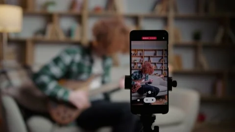Red-haired curly-haired man sits on the sofa and plays the guitar Stock Footage 233260783