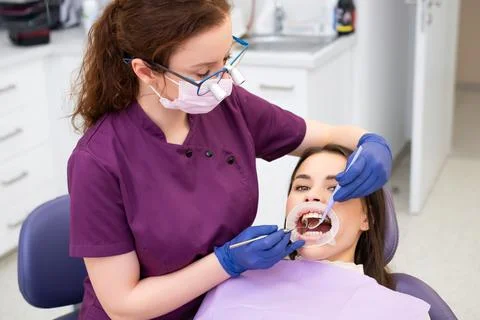 Red haired dentist in glasses performs examination of teeth of brunette female Stock Photos