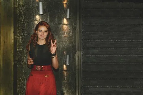 Red haired event host with a microphone in a room with lanterns and a gray wall Foto stock