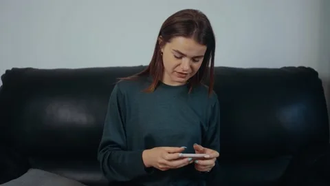The red-haired, freckled, focused young woman is playing on the phone, sitting Stock Footage 163758423