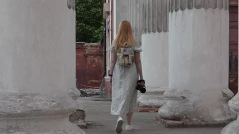 A red-haired girl with a camera in her hands walks along the ancient columns Stock Footage 277139529