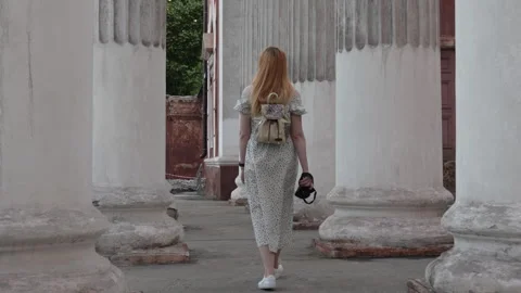 A red-haired girl with a camera in her hands walks along the ancient columns. Stock Footage 280048344