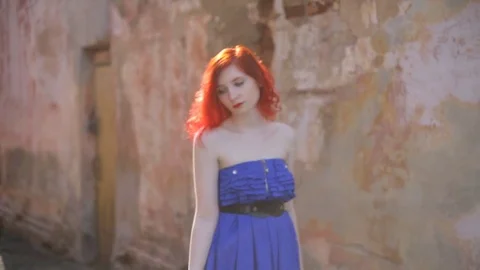 Red-haired girl dancing on wall background. A woman in a blue light dress w.. Video stock 73024845