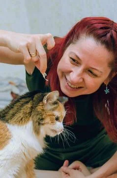 Red-haired girl feeding her cat, cat catching food and eating. Closeup. Stock Photos