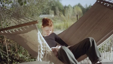 Red-haired girl lying in a hammock relazing and looking at the phone. Stock Footage 286204558