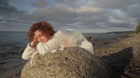 Red-haired girl is lying on a large rock on the beach. Stock Footage 78710529