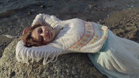 Red-haired girl is lying on a large rock on the beach. Video stock 78723541