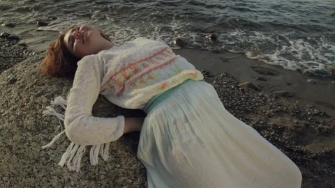 Red-haired girl is lying on a large rock on the beach. Stock Footage 78724498