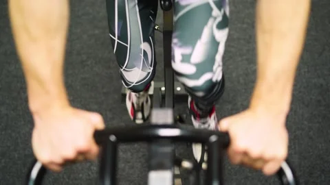 Red-haired guy in black pants rides a bicycle in the gym. close-up of a hand 動画素材 163460509