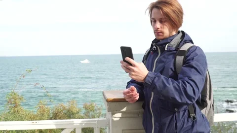 Red-haired guy in a blue jacket on the background of the sea makes a selfie Vidéo 163446367