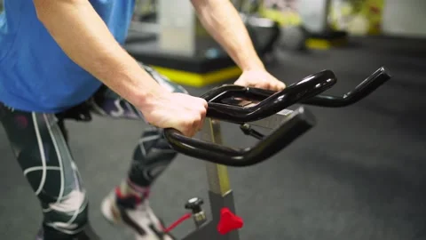 Red-haired guy in a blue t-shirt rides a bicycle in the gym. close-up of a hand Stock-Footage 163458847